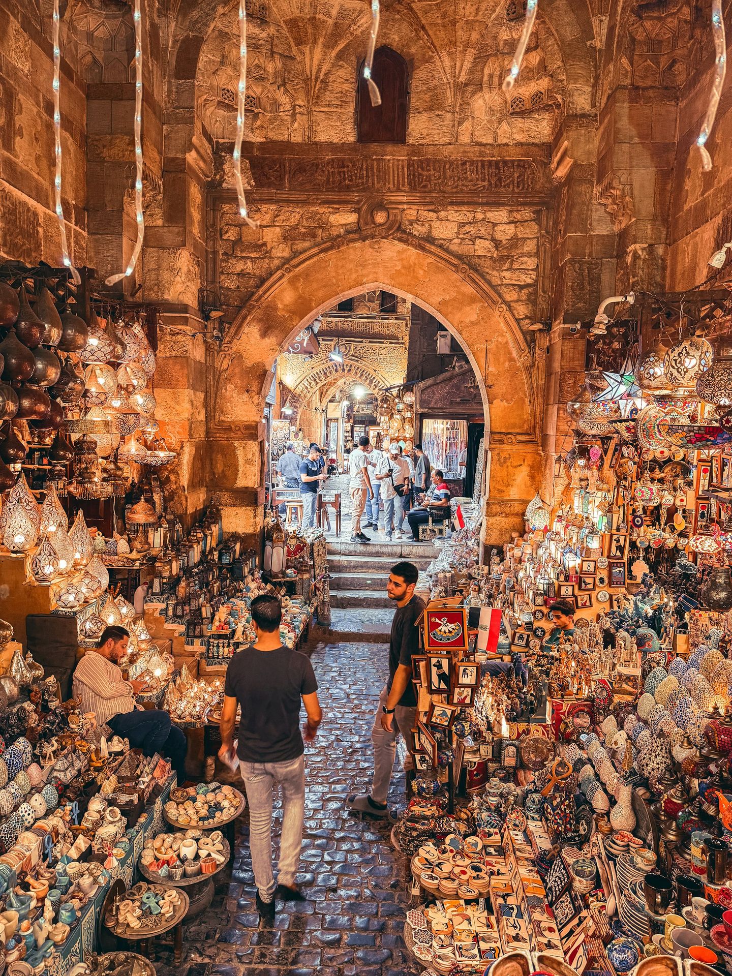 Two men walking through a market filled with lots of items